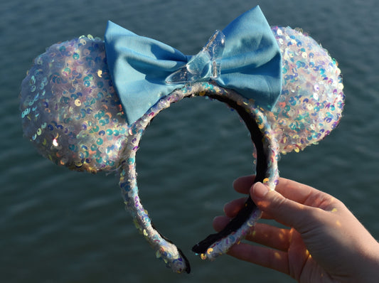 White sequin Disney ears, featuring a light blue bow and a glass slipper attached to middle of the bow.